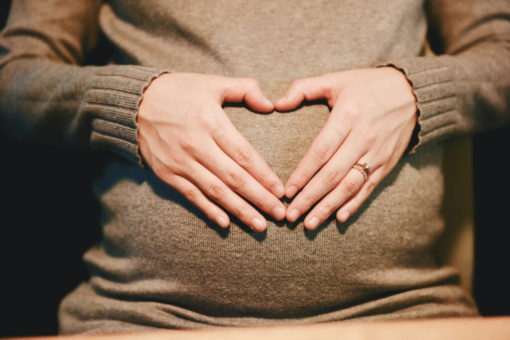 Women creating a heartshape with hands over her pregnancy bump. Photo Credit: Suhyeon Choi on Unsplash