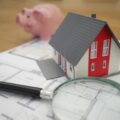 Photograph of a piggy bank, a small plastic house and a magnifying glass