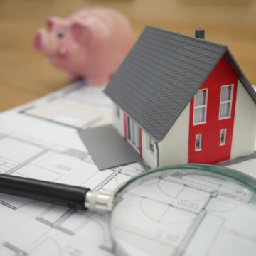 Photograph of a piggy bank, a small plastic house and a magnifying glass