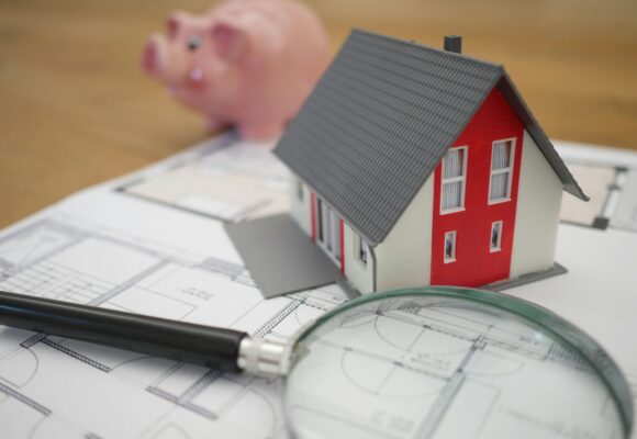 Photograph of a piggy bank, a small plastic house and a magnifying glass
