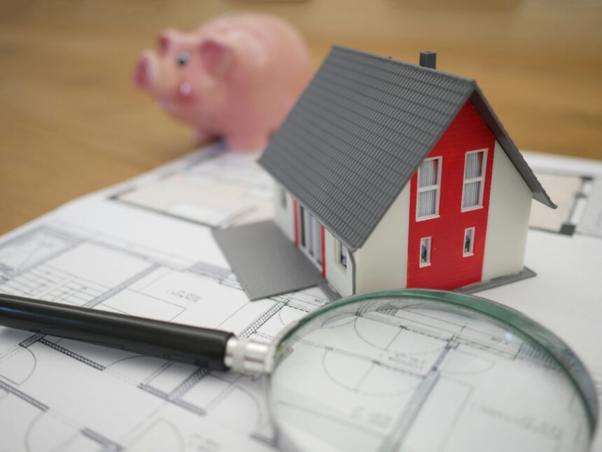 Photograph of a piggy bank, a small plastic house and a magnifying glass