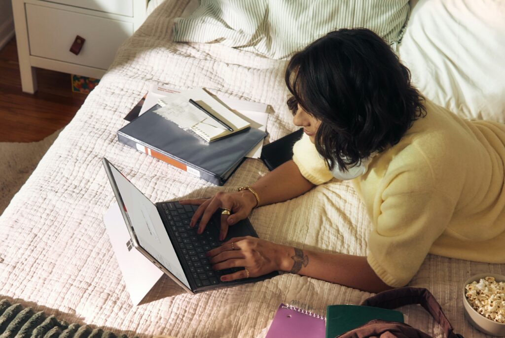 A girl working on her laptop on her bed.