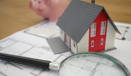 Photograph of a piggy bank, a small plastic house and a magnifying glass